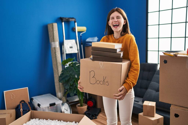 Jeune femme brune se déplaçant vers une nouvelle maison tenant boîte sourire et rire dur à haute voix parce que drôle blague folle.  - Photo, image