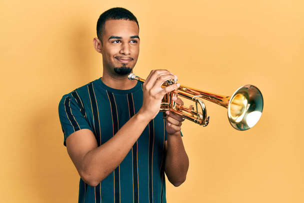 Young african american man playing trumpet smiling looking to the side and staring away thinking.  - Zdjęcie, obraz