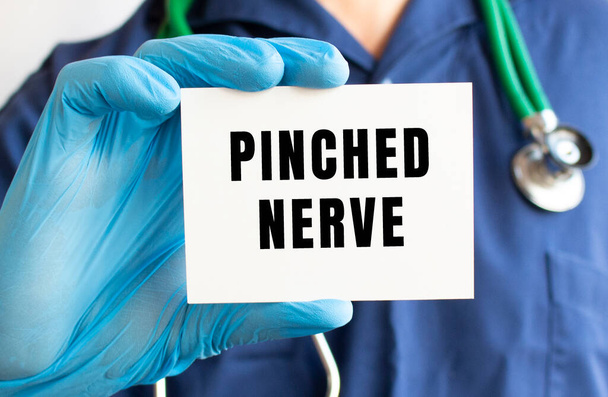 Un médico con un traje médico azul sostiene una tarjeta con el texto NERVIO PINCHADO. - Foto, Imagen