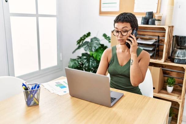 Giovane donna ispanica che parla sullo smartphone che lavora in ufficio - Foto, immagini