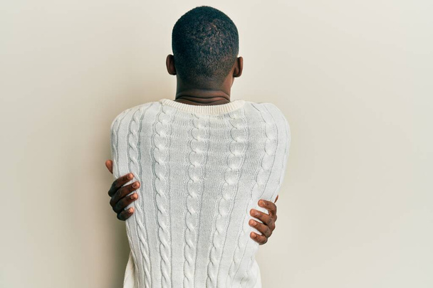 Νεαρός Αφροαμερικάνος που φοράει καθημερινά ρούχα αγκαλιάζοντας τον εαυτό του χαρούμενος και θετικός από πίσω. αυτοαγάπη και αυτοφροντίδα  - Φωτογραφία, εικόνα