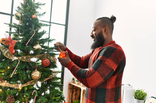 Junger afrikanisch-amerikanischer Mann lächelt selbstbewusst Weihnachtsbaum zu Hause schmücken - Foto, Bild