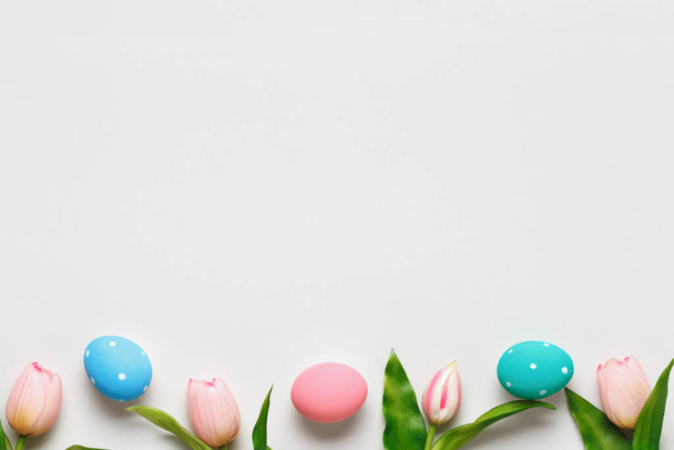 Easter composition on a gray pastel background. Tulips and colored eggs. Border flat lay top view copy space - Photo, image