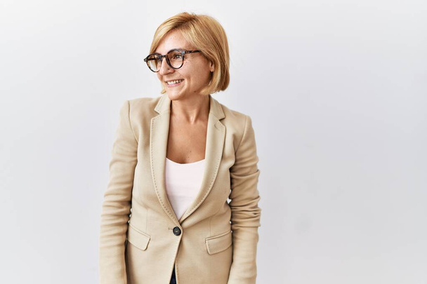 Middle age blonde business woman standing over isolated background looking away to side with smile on face, natural expression. laughing confident.  - Photo, Image