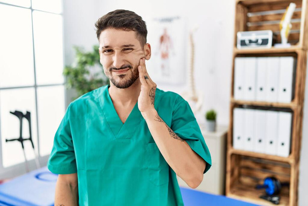 Young physiotherapist man working at pain recovery clinic touching mouth with hand with painful expression because of toothache or dental illness on teeth. dentist  - Foto, immagini