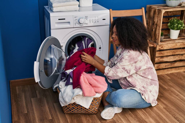 Молодая африканская американка улыбается уверенно стирая одежду в прачечной - Фото, изображение