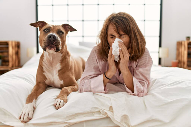 Joven mujer caucásica enfermedad usando servilleta acostado en la cama con perro en el dormitorio - Foto, Imagen