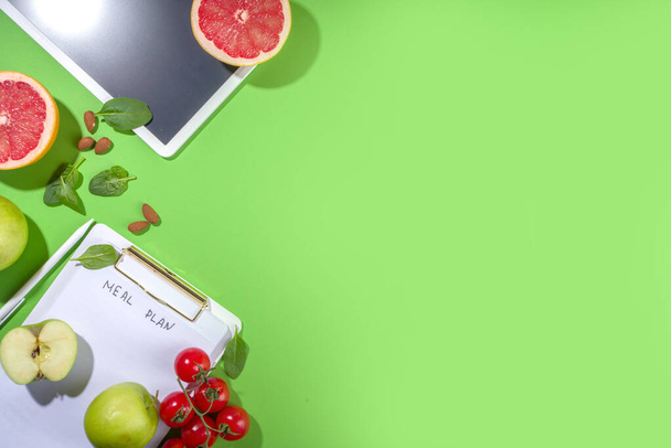 Comida concepto plan de dieta, con bloc de notas, frutas alimentos saludables, verduras, tabletas, cuadernos y accesorios para adelgazar sobre fondo de mesa verde brillante - Foto, Imagen