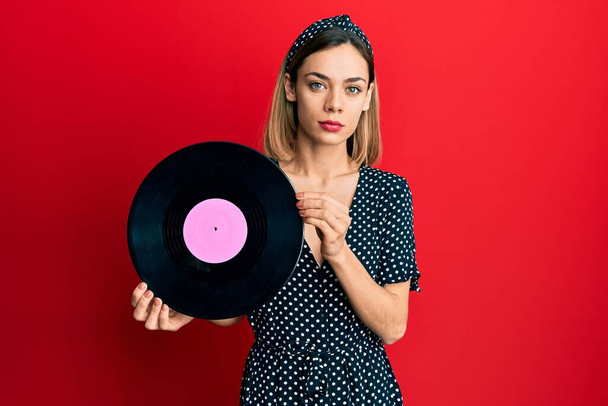 Young caucasian blonde woman holding vinyl disc relaxed with serious expression on face. simple and natural looking at the camera.  - Fotografie, Obrázek