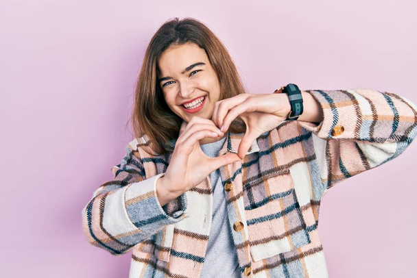 Fiatal kaukázusi lány alkalmi ruhát visel mosolyogva a szerelemben csinál szív szimbólum alakú kezekkel. romantikus koncepció.  - Fotó, kép