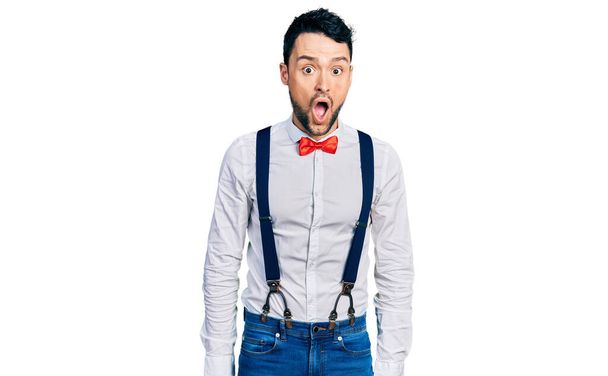 Hispanic man with beard wearing hipster look with bow tie and suspenders afraid and shocked with surprise expression, fear and excited face.  - Photo, Image