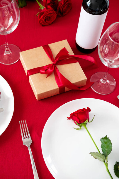 Romantic dinner table setting for Valentines Day. Rose flower on plate, gift box, bottle of win, glasses. - 写真・画像