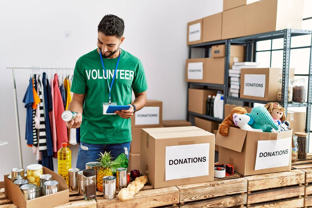 Jonge Arabier man draagt vrijwilliger uniform met behulp van touchpad in het liefdadigheidscentrum - Foto, afbeelding