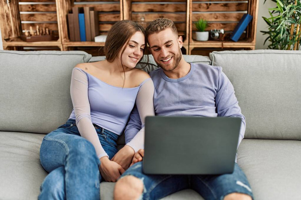 Giovane coppia caucasica utilizzando il computer portatile seduto sul divano a casa. - Foto, immagini