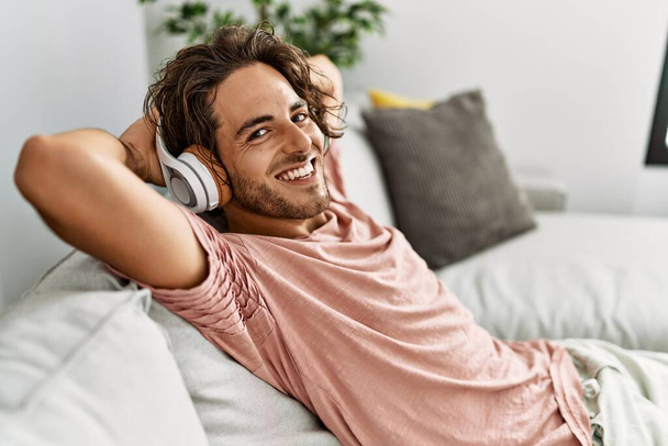 Giovane uomo ispanico rilassato con le mani sulla testa ascoltando musica a casa. - Foto, immagini