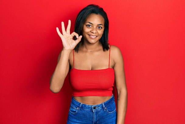 Young african american girl wearing casual style with sleeveless shirt smiling positive doing ok sign with hand and fingers. successful expression.  - Foto, immagini