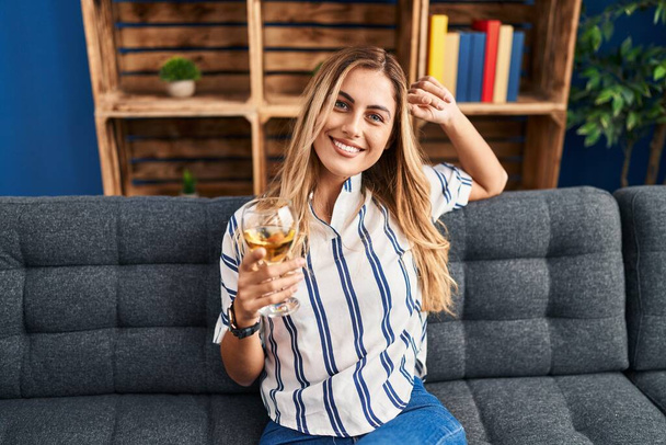 Young blonde woman drinking champagne sitting on sofa at home - Foto, Imagem