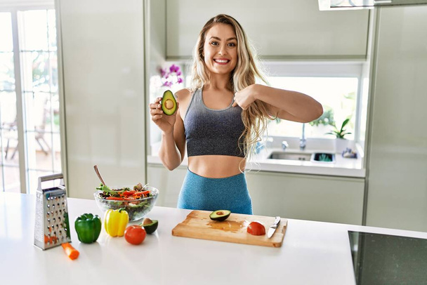 Young caucasian fitness woman wearing sportswear preparing healthy salad at the kitchen pointing finger to one self smiling happy and proud  - Foto, immagini