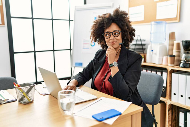 African american woman with afro hair working at the office wearing operator headset with hand on chin thinking about question, pensive expression. smiling and thoughtful face. doubt concept.  - Foto, Imagem