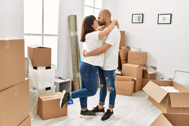 Young hispanic couple kissing and hugging moving at new home. - 写真・画像