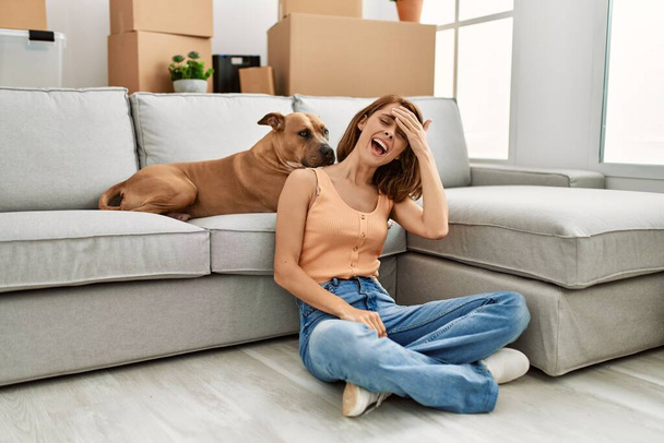 Young caucasian girl wearing casual clothes sitting on the floor with dog at home stressed and frustrated with hand on head, surprised and angry face  - Φωτογραφία, εικόνα