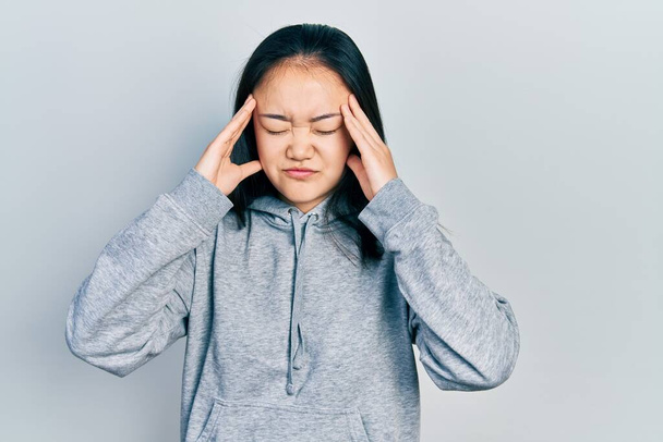 Giovane ragazza cinese indossa abiti casual che soffrono di mal di testa disperato e stressato perché il dolore e l'emicrania. mani sulla testa.  - Foto, immagini