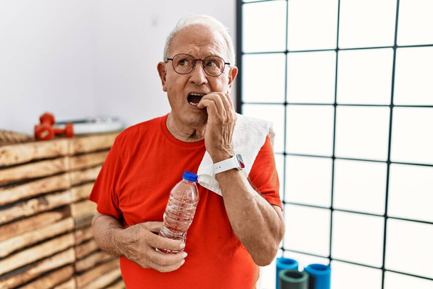 Senior man wearing sportswear and towel at the gym looking stressed and nervous with hands on mouth biting nails. anxiety problem.  - Photo, Image