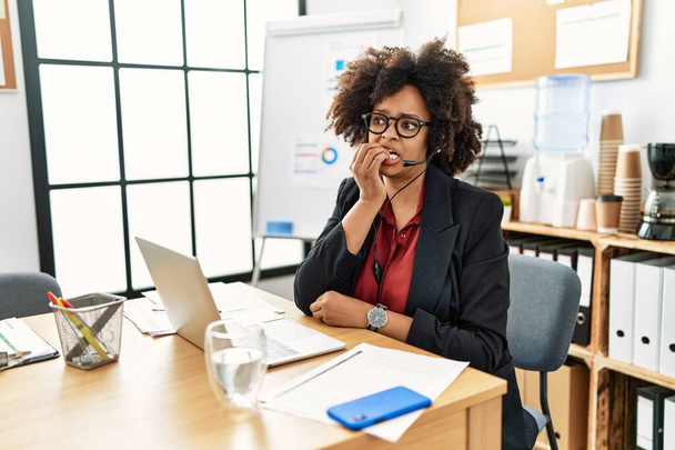 African american woman with afro hair working at the office wearing operator headset looking stressed and nervous with hands on mouth biting nails. anxiety problem.  - Foto, afbeelding