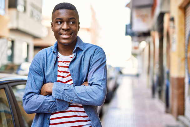 Nuori afrikkalainen amerikkalainen mies hymyilee tyytyväisenä kädet ristissä ele kaupungin. - Valokuva, kuva