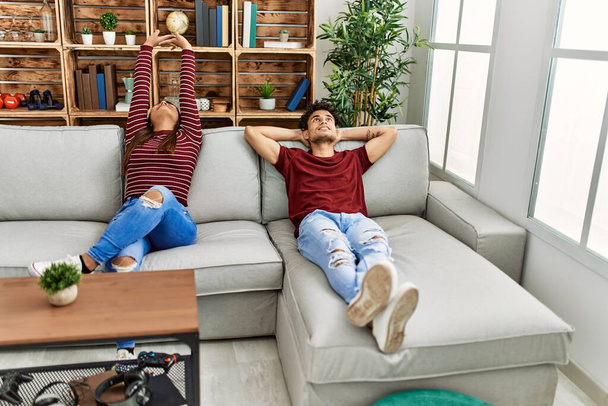 Fiatal latin pár fáradt ásítás és kinyújtott karok ül a kanapén otthon. - Fotó, kép