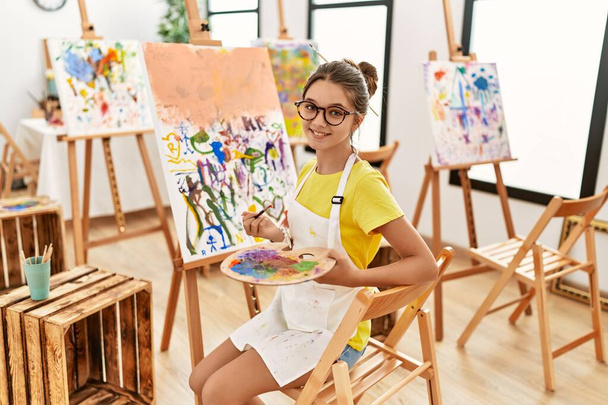 Очаровательная девушка улыбается уверенно рисуя в художественной студии - Фото, изображение