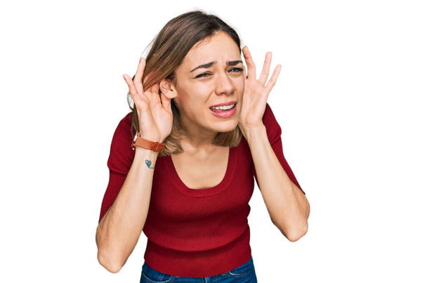 Menina loira jovem vestindo roupas casuais tentando ouvir ambas as mãos no gesto da orelha, curioso para fofocas. problema auditivo, surdo  - Foto, Imagem
