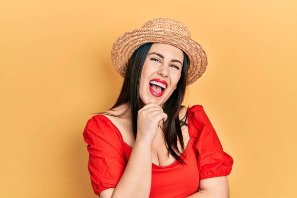 Young hispanic woman wearing summer hat looking confident at the camera smiling with crossed arms and hand raised on chin. thinking positive.  - Foto, imagen