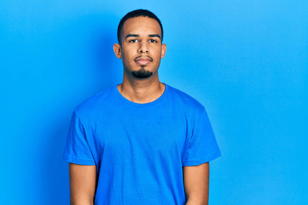 Young african american man wearing casual blue t shirt relaxed with serious expression on face. simple and natural looking at the camera.  - Фото, изображение