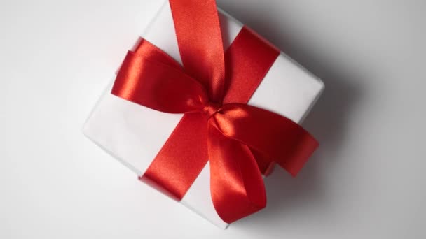 Rotate white gift box with red ribbon on white background with place for your text. Video motion on Valentines Day, mothers day or Birthday. Top view 4k footage - Video