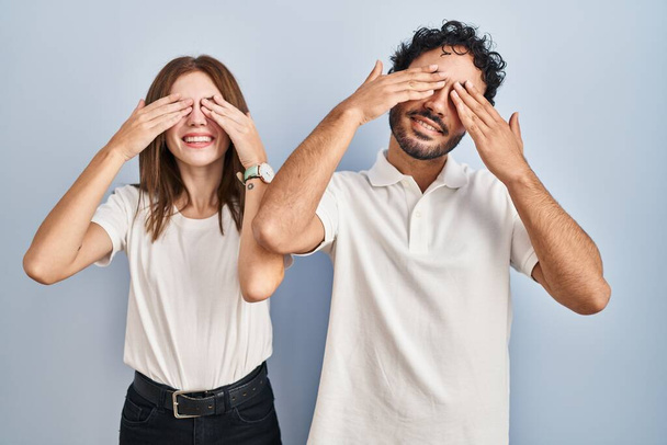 Young couple wearing casual clothes standing together covering eyes with hands smiling cheerful and funny. blind concept.  - Фото, изображение