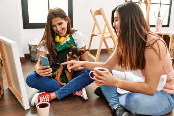 Dva latinsky malovat studenty pití kávy a pomocí smartphone se psem na umělecké škole. - Fotografie, Obrázek