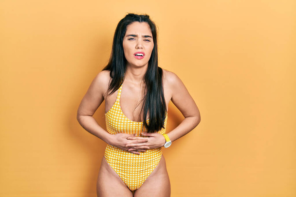 Young hispanic girl wearing swimsuit with hand on stomach because indigestion, painful illness feeling unwell. ache concept.  - Fotografie, Obrázek