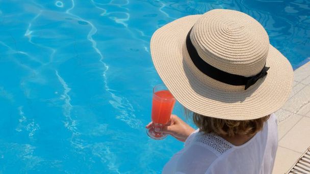 hembra en un sombrero de paja se relaja cerca de la piscina, bebe un cóctel rosa, de cerca. Concepto de humor de verano - Foto, Imagen