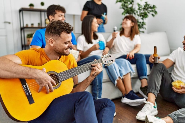 Groupe de jeunes amis sur la fête souriant heureux et jouer de la guitare classique à la maison. - Photo, image