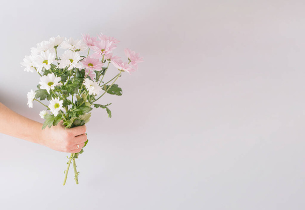 Creative spring arrangement made of a bouquet of flowers in hand on a gray background. Minimal concept with copy space. - Фото, изображение