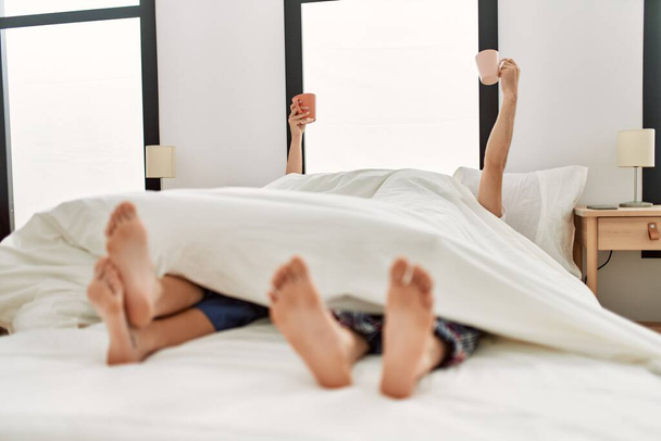 Um casal acordado debaixo do cobertor. Tomar café da manhã segurando xícara de café levantado na cama. - Foto, Imagem