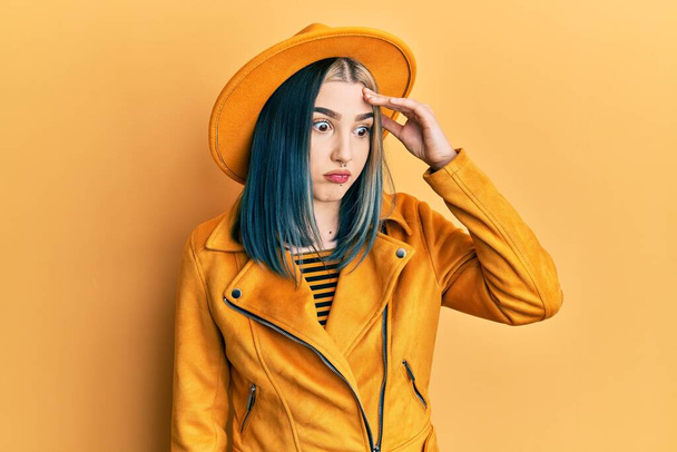 Jong modern meisje draagt gele hoed en leren jas bezorgd en gestrest over een probleem met de hand op het voorhoofd, nerveus en angstig voor crisis  - Foto, afbeelding