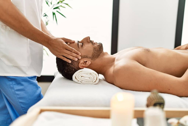Dos hombres hispanos terapeuta y paciente teniendo masaje facial en el centro de belleza - Foto, Imagen