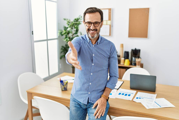 Middle age hispanic man with beard wearing business clothes at the office smiling friendly offering handshake as greeting and welcoming. successful business.  - Photo, image