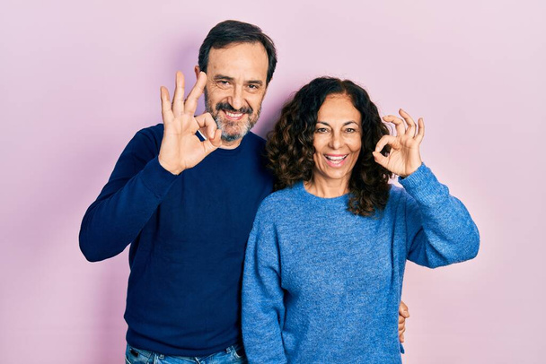 Middle age couple of hispanic woman and man hugging and standing together smiling positive doing ok sign with hand and fingers. successful expression.  - Photo, Image