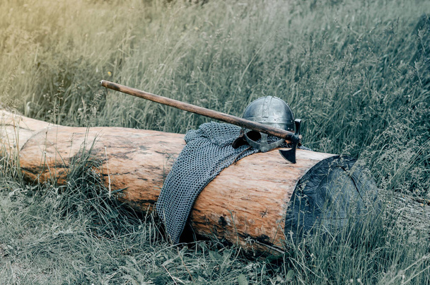 Metal chain mail, helmet and ax lie on  wooden log. Viking armor. Historical film concept. - Photo, Image