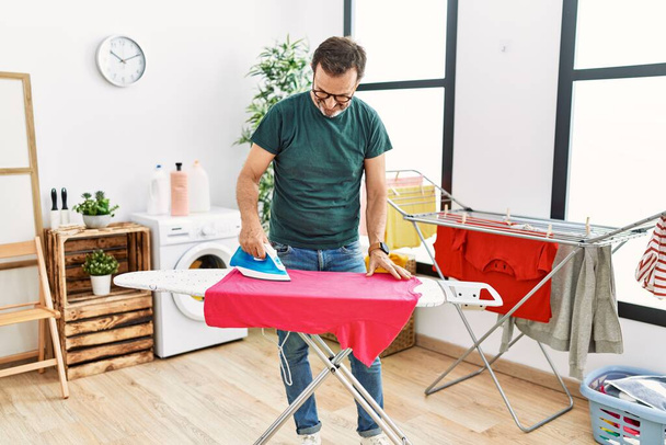 Hombre hispano de mediana edad planchando ropa en casa. - Foto, imagen