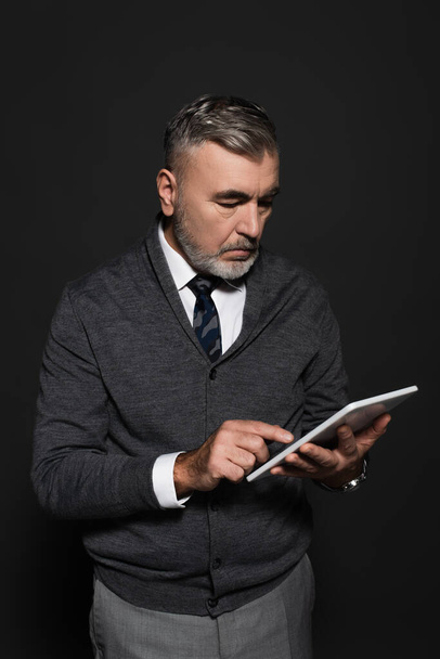 grey-haired man in stylish clothes using digital tablet on dark grey - Foto, afbeelding