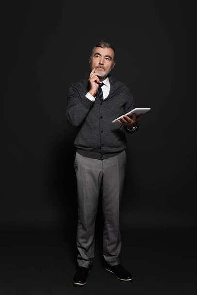 full length view of pensive senior man with digital tablet looking away on dark grey - Fotó, kép